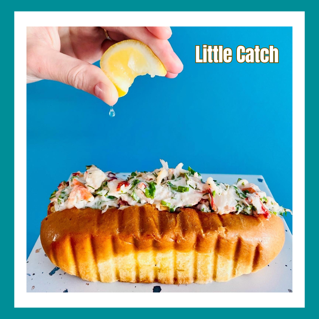 a hand squirting lemon juice on a lobster roll